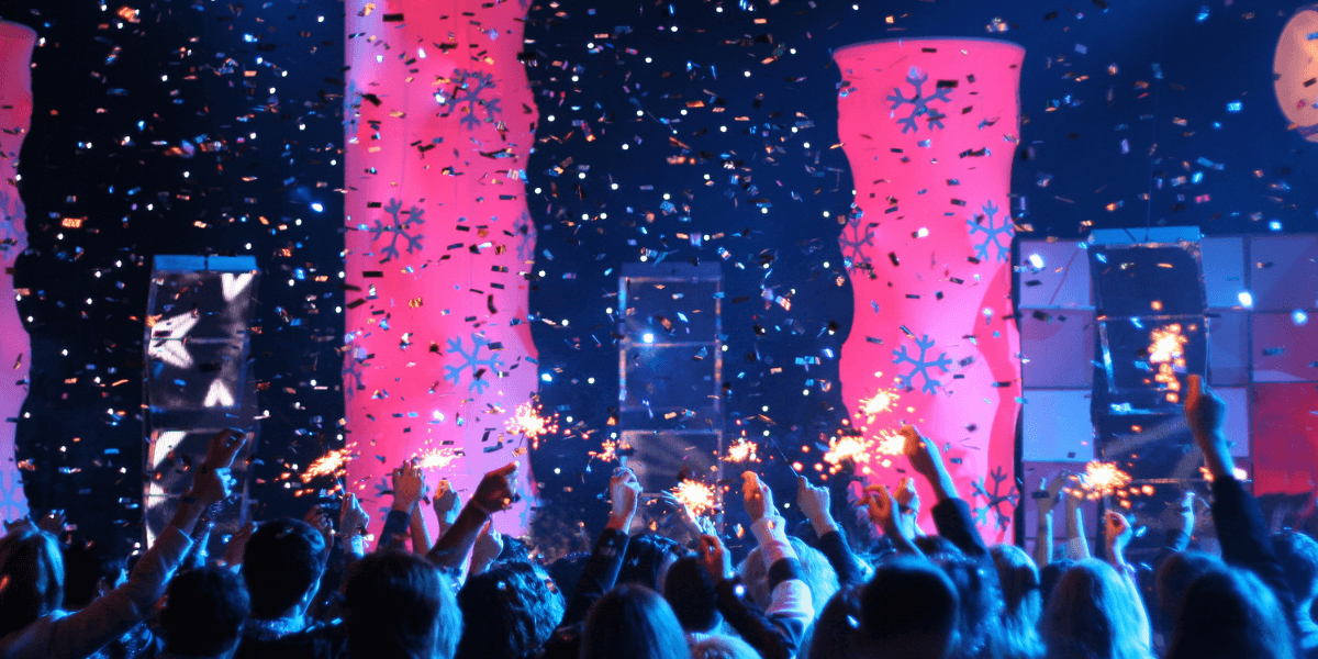 Crowd celebrating with sparklers and confetti under colorful lighting at an event