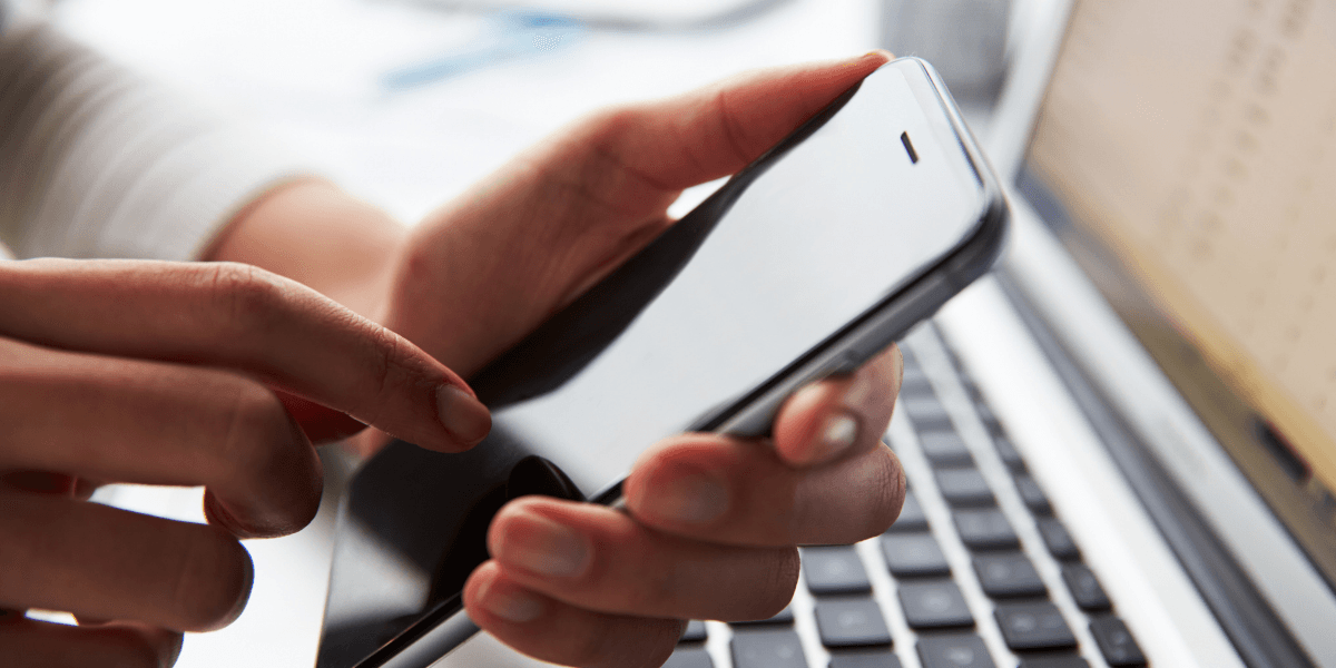 A person using a smartphone while sitting next to a laptop on a desk