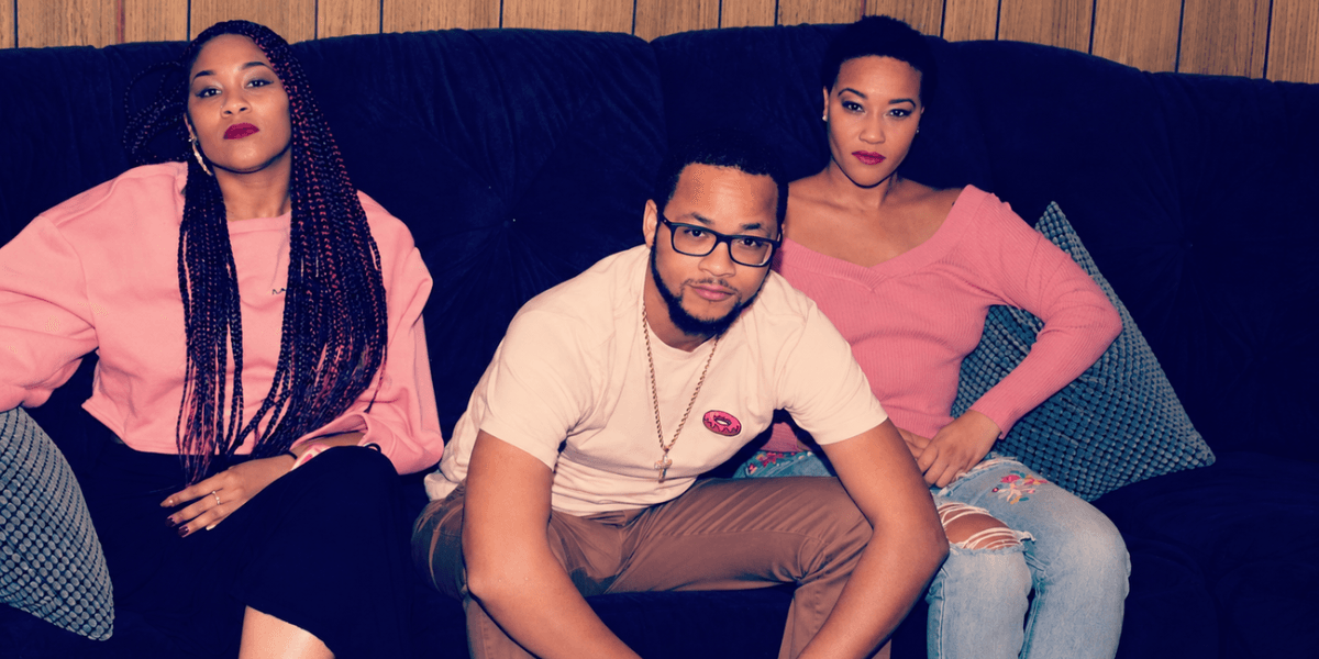 Three individuals posed on a couch, wearing casual clothing in a relaxed setting