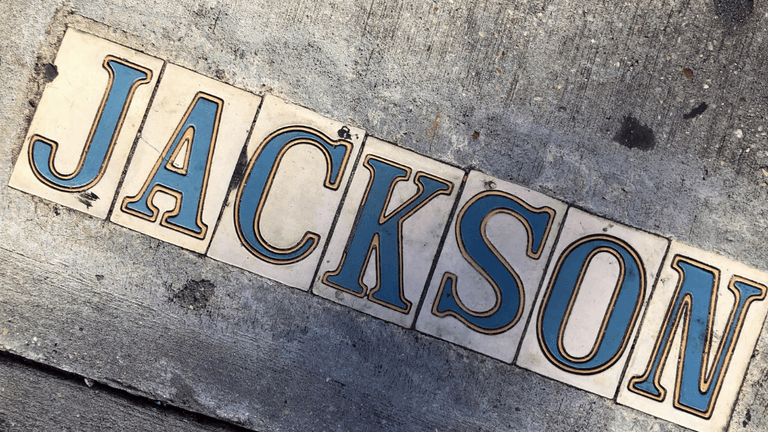 Decorative sidewalk tiles spelling “JACKSON” embedded in a concrete pavement.
