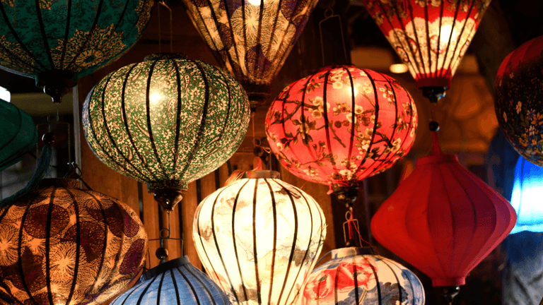 Colorful decorative lanterns hanging indoors with illuminated patterned fabric shades.