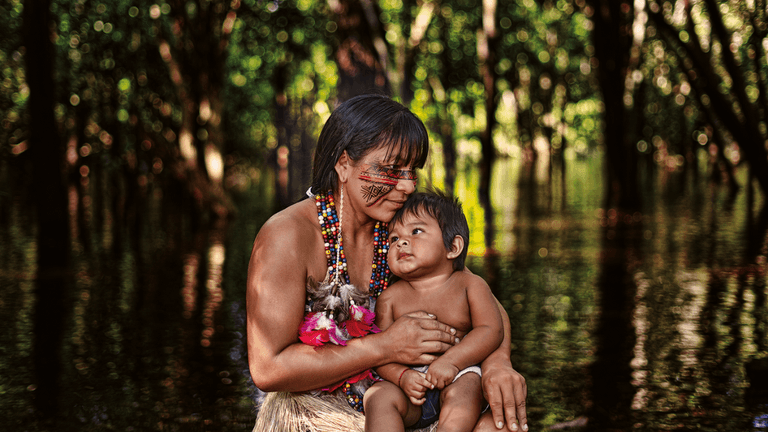 A mother holding her child in the forest, showcasing indigenous culture with symbolic body art and vibrant attire