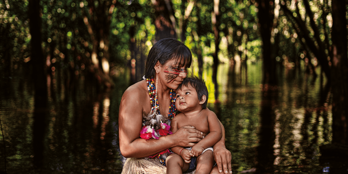 A mother holding her child in the forest, showcasing indigenous culture with symbolic body art and vibrant attire