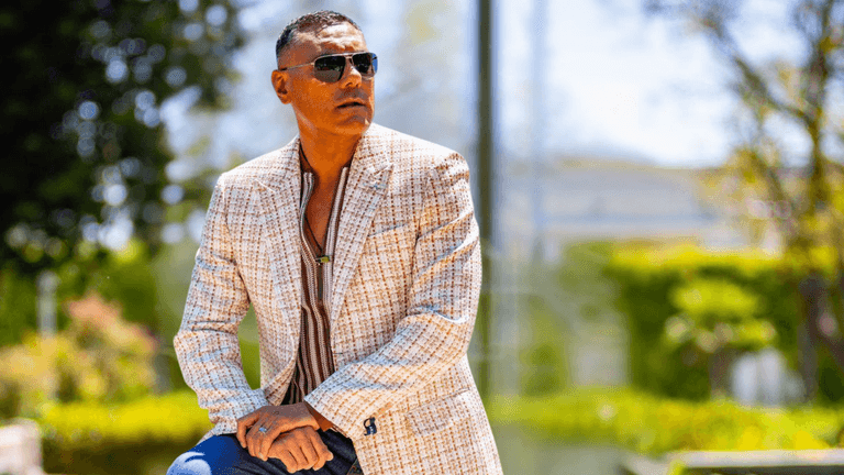 Dylan Garcia in a stylish cream and brown checkered blazer, looking confident and fashionable outdoors with sunglasses.