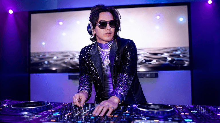 A DJ in sunglasses performs on turntables under purple lights with a digital backdrop