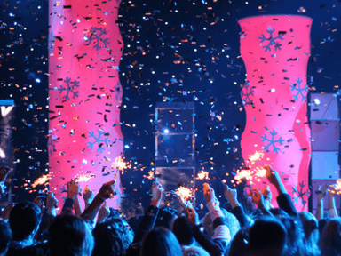 Crowd celebrating with sparklers and confetti under colorful lighting at an event