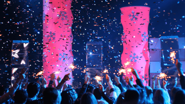 Crowd celebrating with sparklers and confetti under colorful lighting at an event