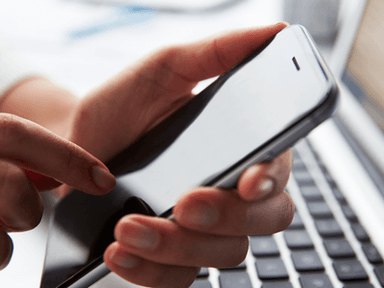 A person using a smartphone while sitting next to a laptop on a desk