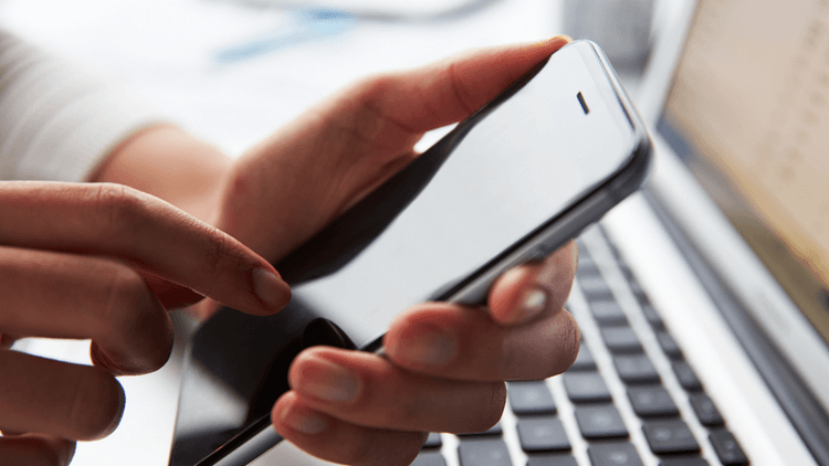 A person using a smartphone while sitting next to a laptop on a desk