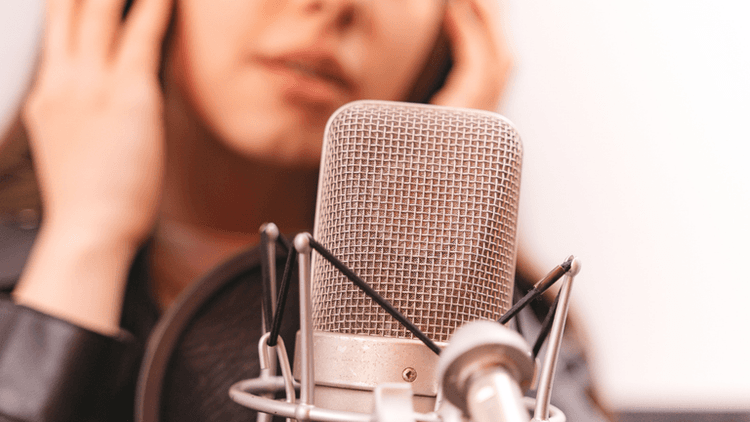 Close-up of a microphone with a blurred person adjusting their headphones in the background