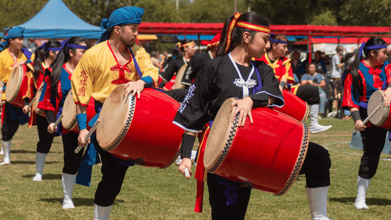 Group of performers drumming in colorful traditional costumes during an outdoor festival