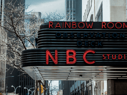 Neon sign for NBC Studios and Rainbow Room above an urban street scene
