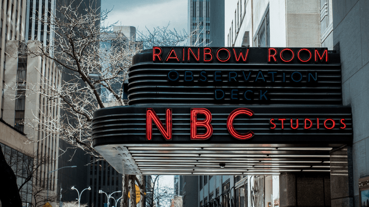 Neon sign for NBC Studios and Rainbow Room above an urban street scene