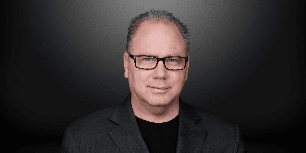 Middle-aged man with glasses and gray hair in a dark blazer against a gray background
