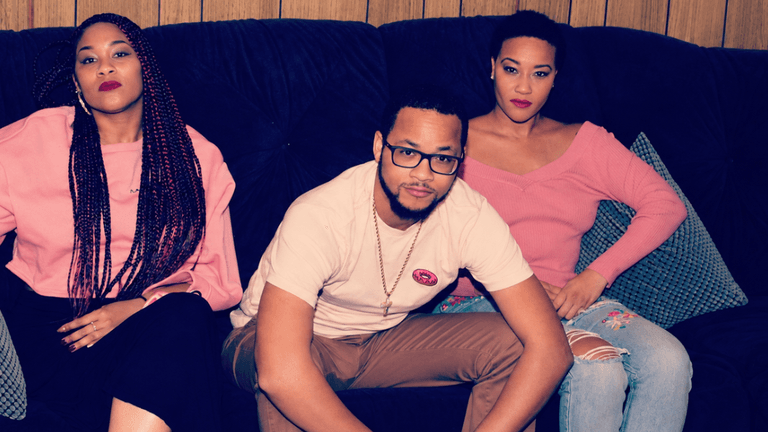 Three individuals posed on a couch, wearing casual clothing in a relaxed setting