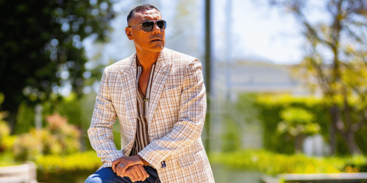 Dylan Garcia in a stylish cream and brown checkered blazer, looking confident and fashionable outdoors with sunglasses.