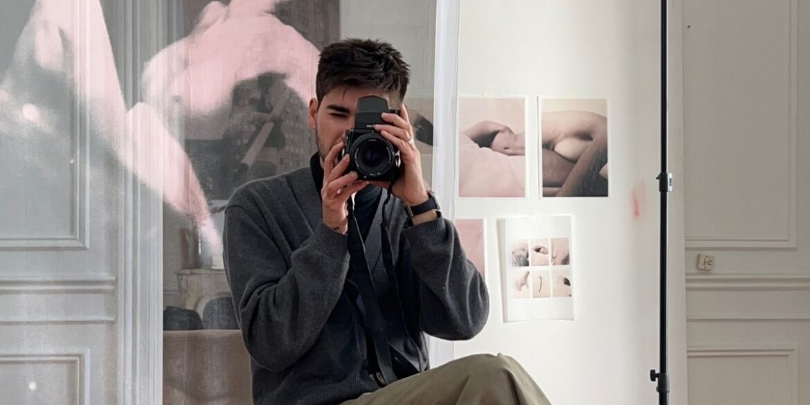 Photographer taking a self-portrait in studio surrounded by artistic nude prints, representing authentic creative expression.