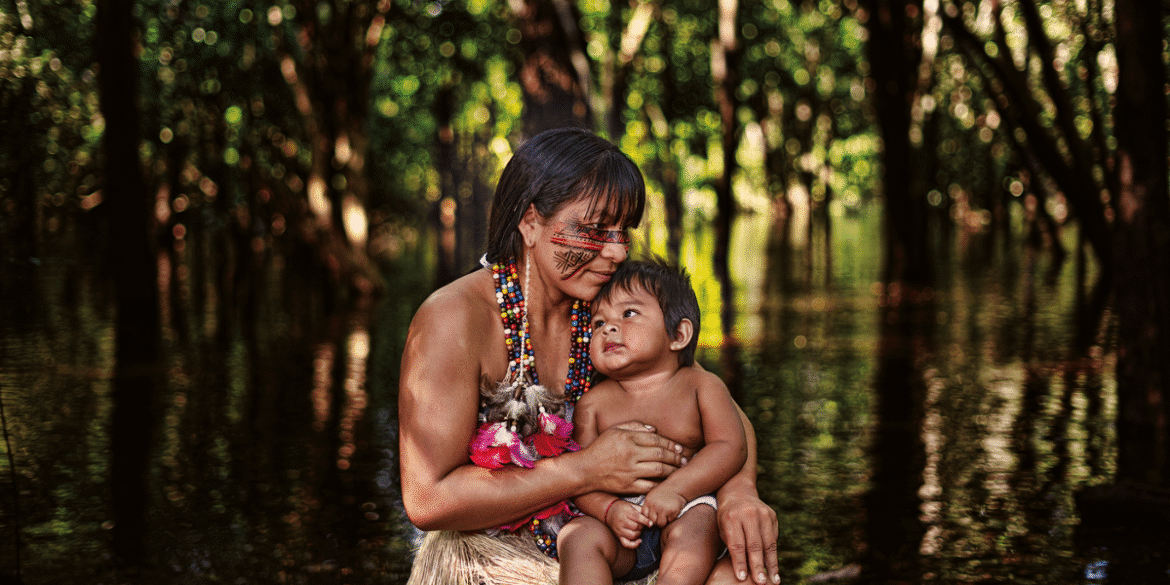A mother holding her child in the forest, showcasing indigenous culture with symbolic body art and vibrant attire