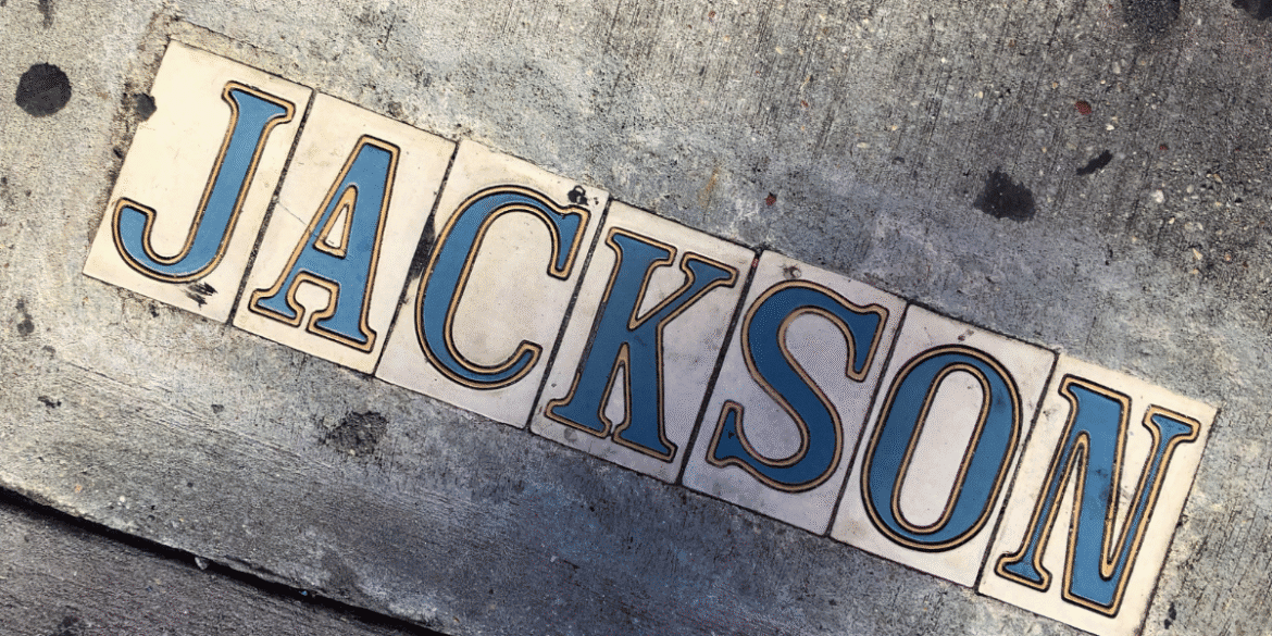 Decorative sidewalk tiles spelling “JACKSON” embedded in a concrete pavement.