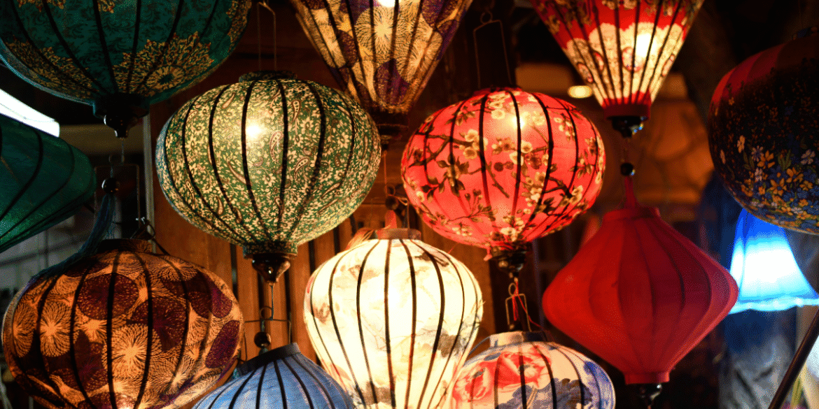 Colorful decorative lanterns hanging indoors with illuminated patterned fabric shades.